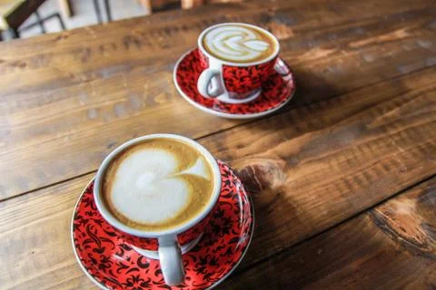 Two red cups of coffee with a pattern and milk foam on wooden table Stock Photos
