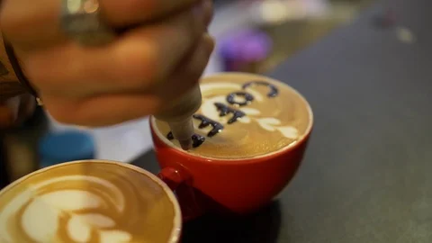 Two red cups of coffee on the table. Barista writes chocolate on one of them. Stock Footage 105878807