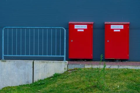 Two red fire boxes next to a gray wall and railing near green grass Stock Photos