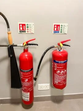 Two red fire extinguishers mounted on a white wall in an indoor setting. Stock Photos