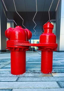 Two red fire hydrants are positioned on the ground outside a large building.  Stock Photos