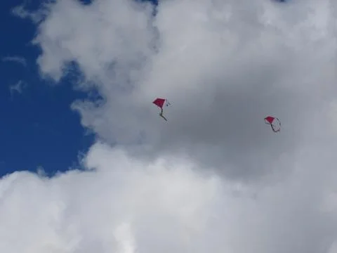 Two red flying kites on a cloudy sky Stock Photos