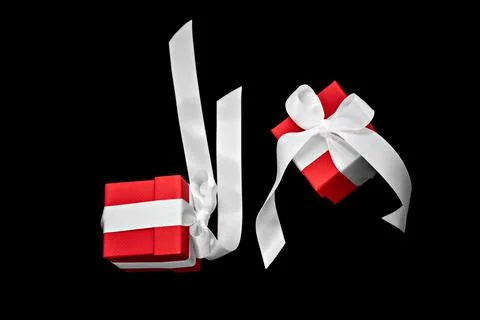 Two red gift boxes with white bows levitate on a black background. Stock Photos