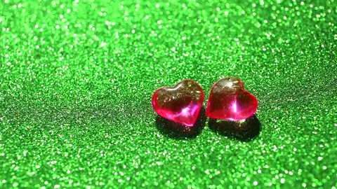 Two red glass hearts revolve in circle on green glittering background Stock Footage 151554913