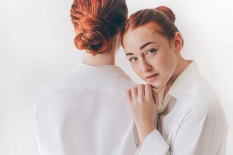 Two red-haired sisters stand isolated on a white background in shirts. One woman Stock Photos