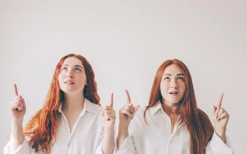 Two red-haired sisters stand isolated on a white background in spacious Stock Photos