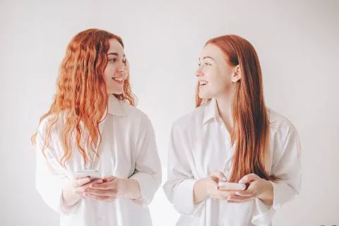 Two red-haired sisters stand isolated on a white background in spacious Stock Photos