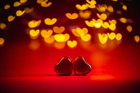 Two red heart-shaped objects rest against a vibrant red background, surrounde Stock Photos