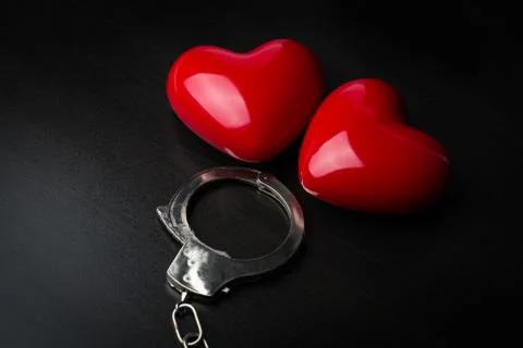 Two red hearts and steel handcuffs on dark background.St Valentine concept Stock Photos
