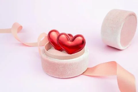 Two red hearts in a ring box with ribbon on soft pink background. Romantic Stock Photos