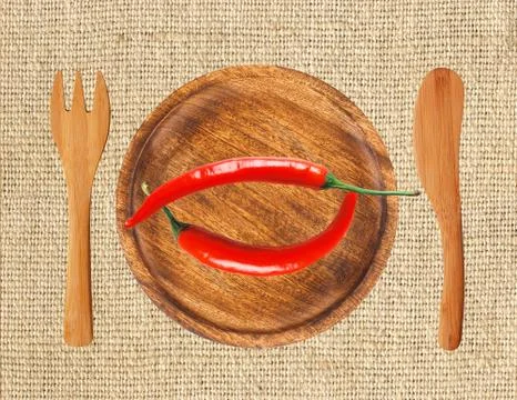 Two red hot chilli peppers on wooden plate over burlap 写真素材
