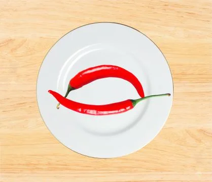 Two red hot chilly peppers on plate on white wooden table Fotos Stock
