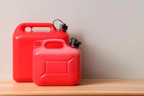 Two red plastic fuel containers on wooden surface with gray background Stock Photos