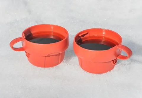 Two Red plastic mugs with black hot tea with steam on a white snow background 스톡 사진