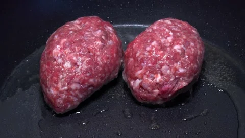 Two red raw meat cutlets in a hot frying pan. Close up view. Stock Footage 157823833