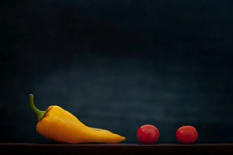 Two red small tomatoes and one large yellow pepper lie in a row on the board. Stock Photos