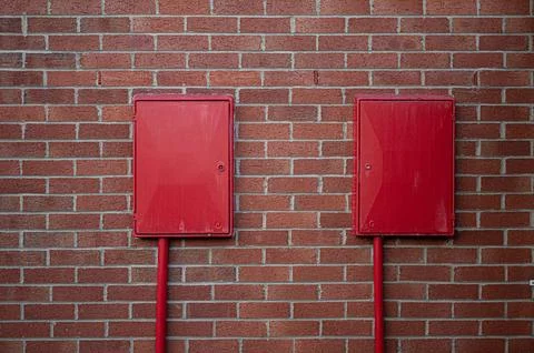 Two red square boxes affixed to a brick wall Stock Photos