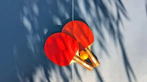 Two Red Table Tennis Rackets And Yellow Ball Lying On Blue Ping Pong Table .. Fotos de archivo