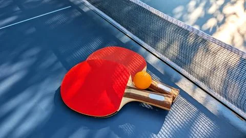 Two Red Table Tennis Rackets And Yellow Ball Lying Near Net On Blue Ping Po.. Фото