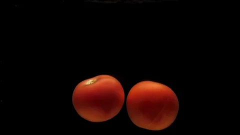 Two red tomatos falling into transparent water on black background Stock Footage 118125602