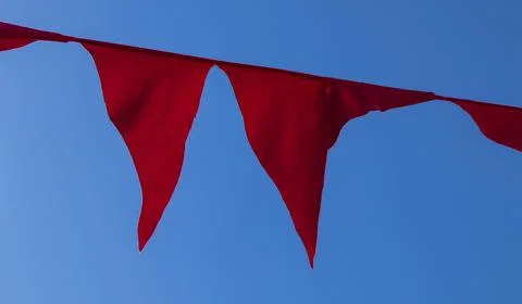 Two red triangular pennants hanging from a string against a blue sky Stock Photos