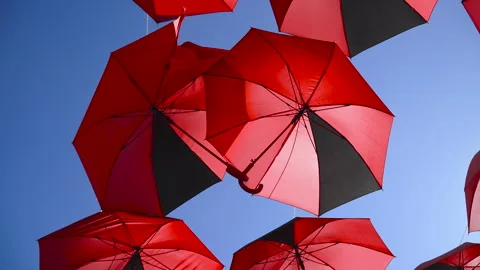 Two red umbrellas, linked by their handles, hover overhead on city street. Vidéo 330534866