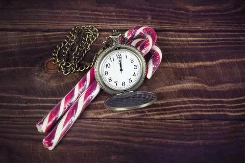 Two red white candy canes and pocket watch on brown wooden surface 写真素材