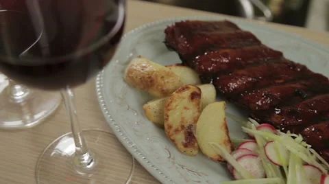 Two red wine glasses, BBQ pork ribs with baked potatoes and coleslaw on plate Stock Footage 46714993