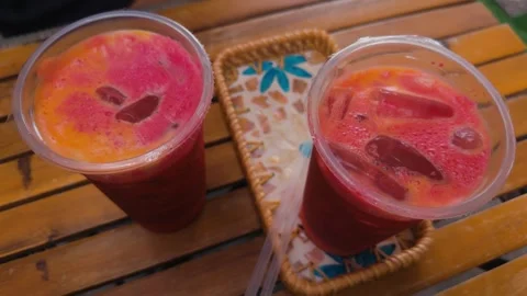 Two refreshing tropical fruit smoothies with ice cubes and a vibrant red and Stock Footage 345515877