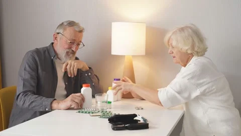 Two retired people sit behind desk discussing medicines, taking pills and drugs Stock Footage 156328366