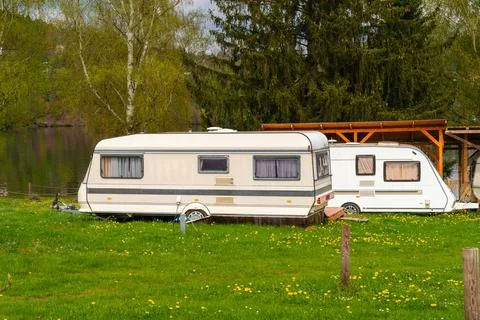 Two retro camper trailers parked on green grass near lake with wooden shelter Stock Photos
