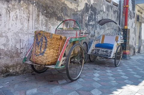 Two rickshaws parked on the sidewalk with a plain and dull wall in the back.. Stock Photos