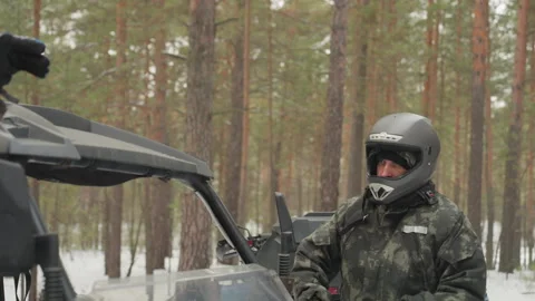 Two riders in snowy pine forest preparing atv expedition camo jackets helmets by Stock Footage 334800503