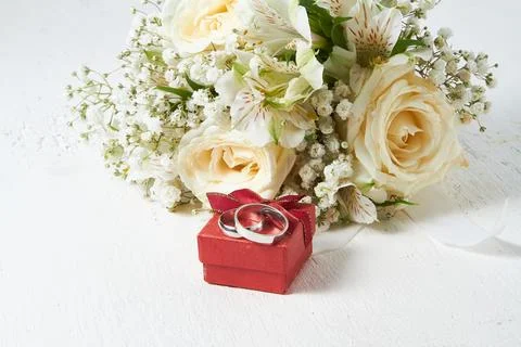 Two rings of different sizes lie on a red box, the bride's bouquet on a whi.. Stock Photos