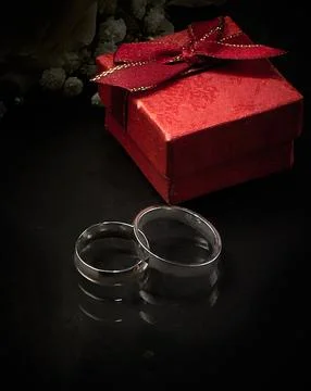Two rings of different sizes, a red gift box lie on a dark background. Photog Stock Photos