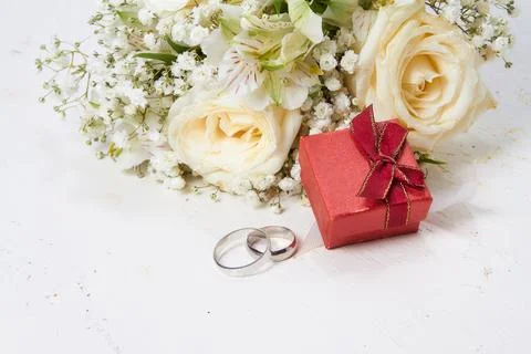Two rings, a gift box in red color, a bouquet of white flowers on a white w.. Stock Photos