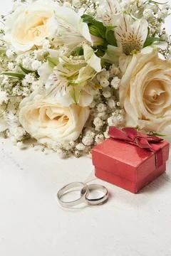 Two rings, a gift box in red color, a bouquet of white flowers on a white w.. Stock Photos