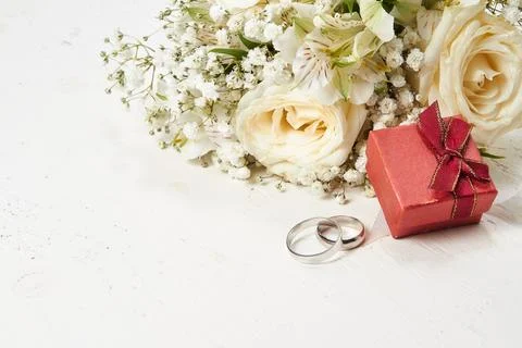 Two rings, red gift box, bouquet of white flowers on white wooden background. Stock Photos