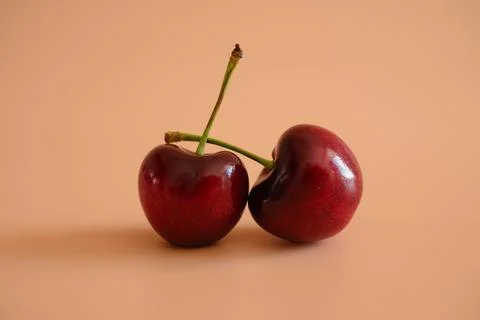 Two ripe cherries on peach background Stock Photos