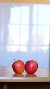 Two ripe red apples lying side by side on a smooth wooden table against a light Stock Photos