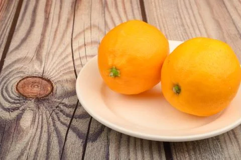 Two ripe yellow lemons on a white plate on a wooden background. Close up. Stock Photos