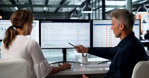 Two Risk Analysts Review Enterprise Strategy On Multiple Computer Screens Tog Stock Photos