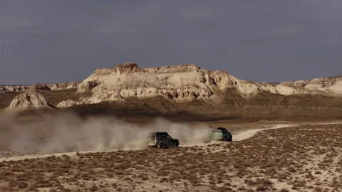 Two off-road vehicles driving fast through a dusty desert landscape of Bozjyra Stock Footage 322039982