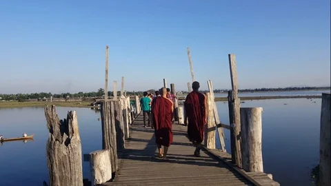 Two robed monks walk across U-Bein Bridge, tourists, boat, river, sky, Mandalay Vídeos de archivo 79423912