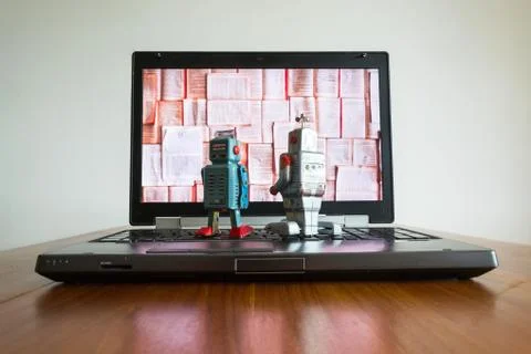 Two robots looking at laptop screen with books Stockfoto's