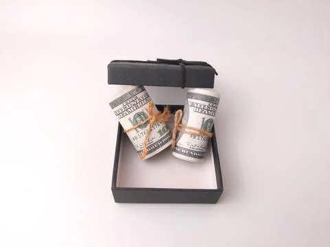 Two rolled US hundred-dollar bills tied with twine sit inside an open black.. Stock Photos