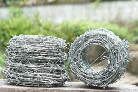Two rolls of galvanized barbed wire placed on wooden surface outdoors with blurr Stock Photos