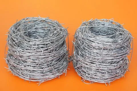 Two rolls of sharp barbed wire placed on a bright orange background, symbolizing Stock Photos