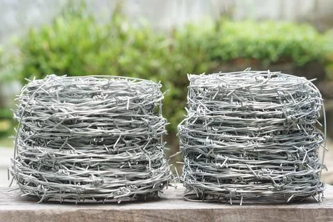 Two rolls of shiny silver barbed wire placed on a wooden surface with blurred gr Stock Photos