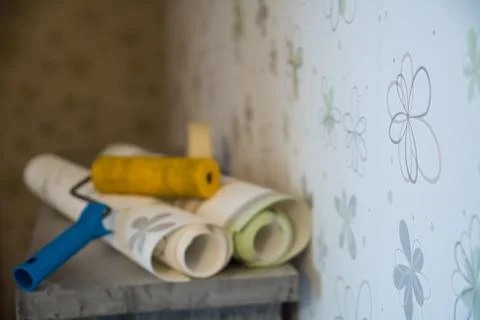 Two rolls of wallpaper and a roller lie against Stock Photos